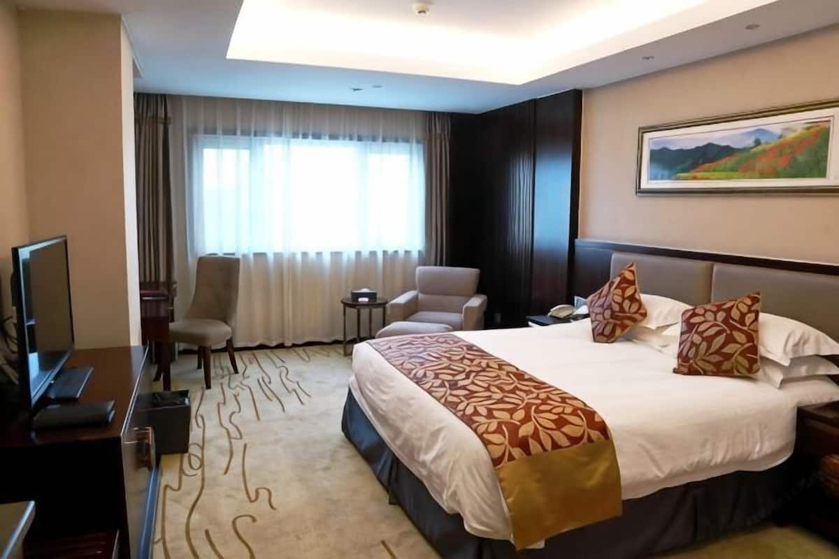 A hotel room with a large bed, a desk with a computer, a chair, a small table, and a television.