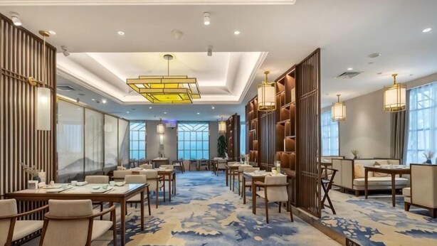 A hotel lobby with multiple seating areas, a patterned carpet, and a large chandelier. - New Era Hotel (Nanjing)