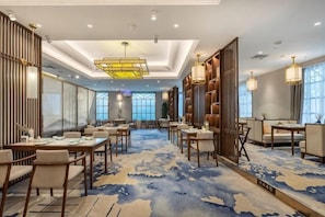 Un hall d’hôtel doté de plusieurs espaces salon, d’un tapis à motifs et d’un grand lustre.