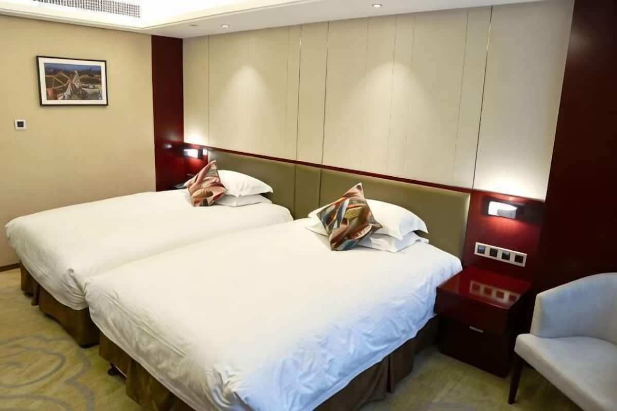 A hotel room with two beds, a nightstand, a chair, and a wall-mounted TV.