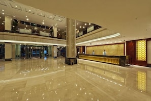 A spacious lobby with a reception desk, a large pillar, and a polished floor. - New Era Hotel (Nanjing)