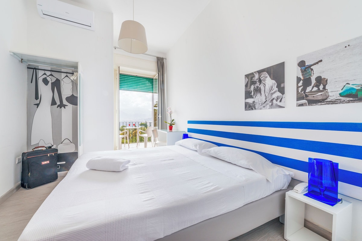 Una habitación de hotel moderna con una cama grande, una mesita de noche con lámpara, un armario y un balcón con vistas.
