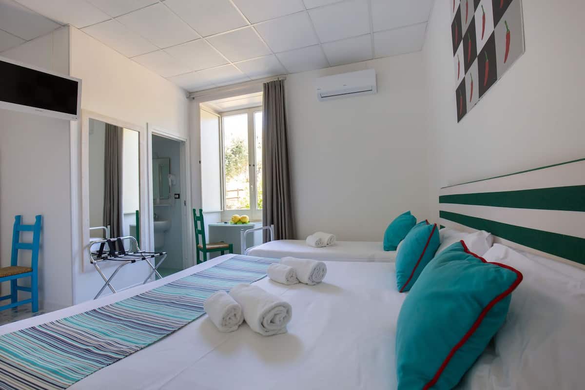 A hotel room with two beds, a window with curtains, a desk with a chair, and a bathroom visible through an open door.