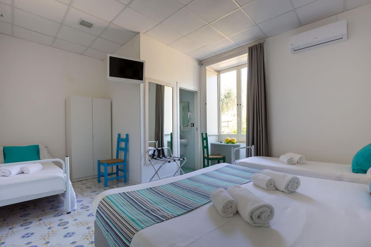 A hotel room with two beds, a desk, a chair, a TV, and a window with curtains.
