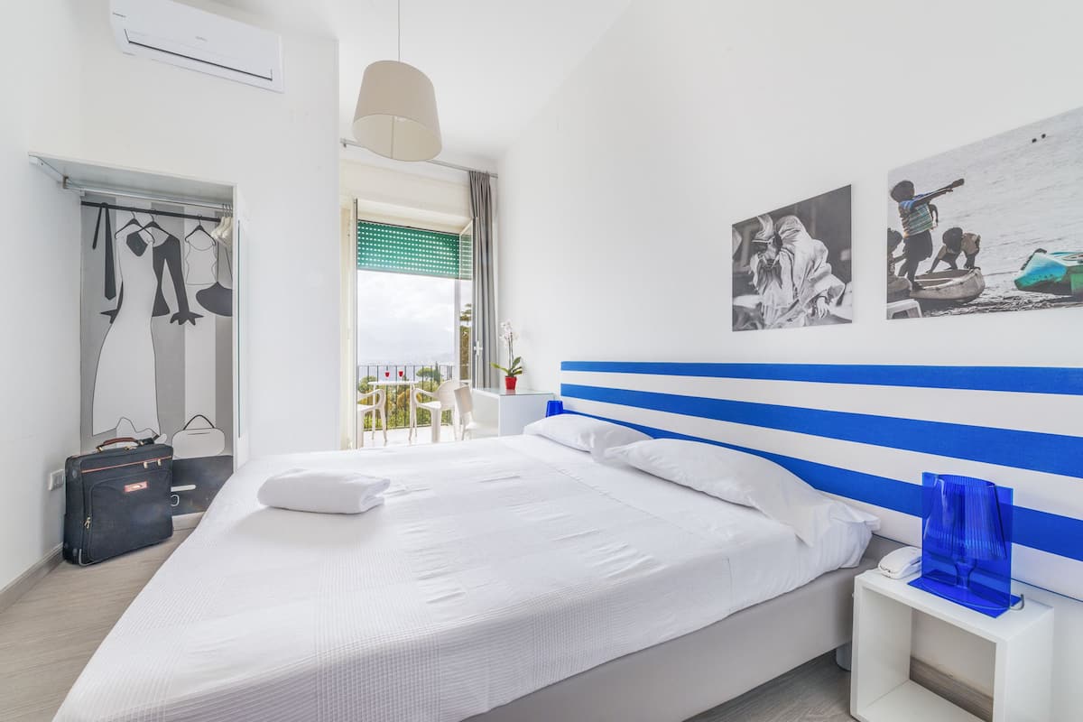 A modern hotel room with a large bed, a white nightstand, and a view of the balcony.