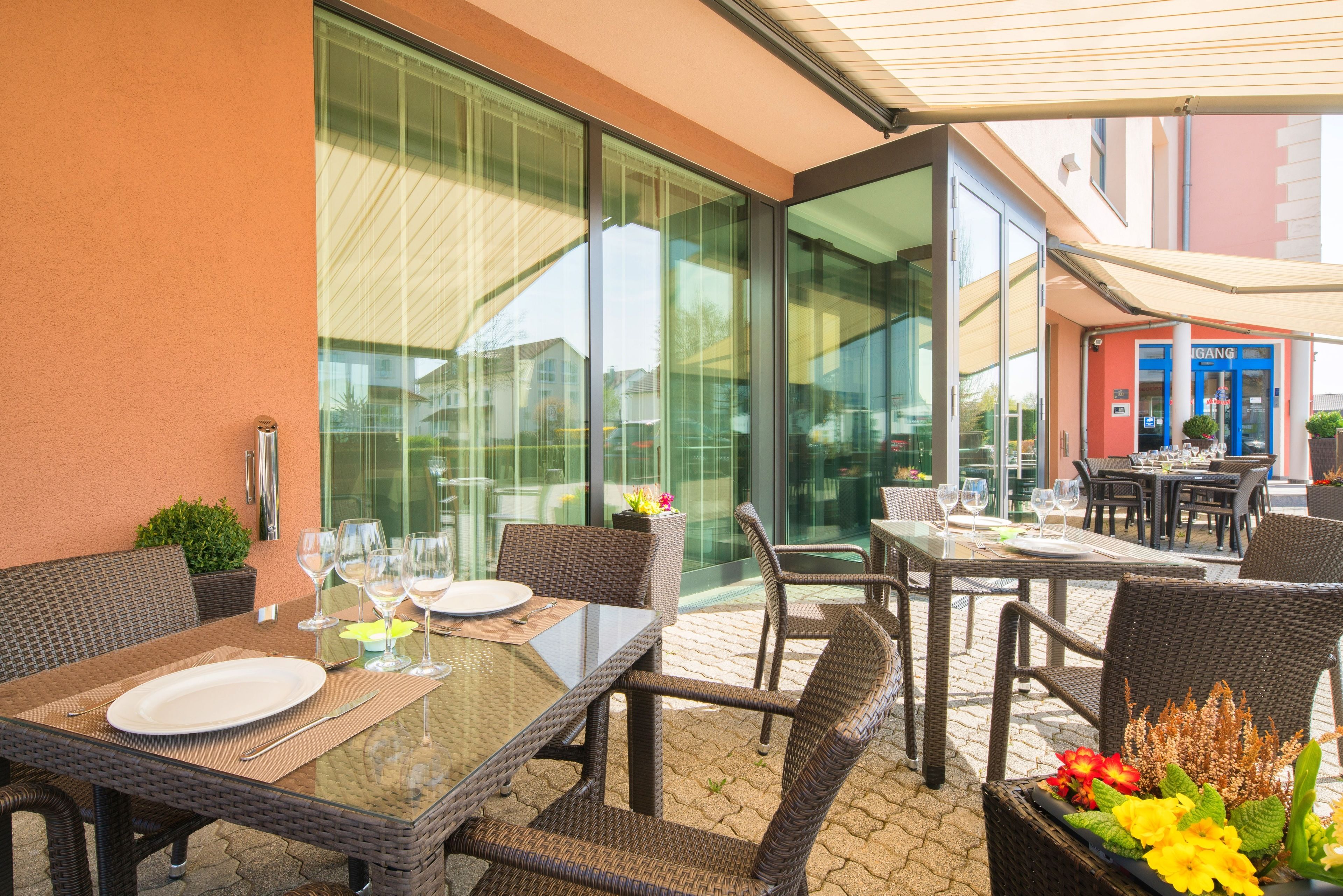 An outdoor dining area with wicker furniture, glass tables, and a view of the street.