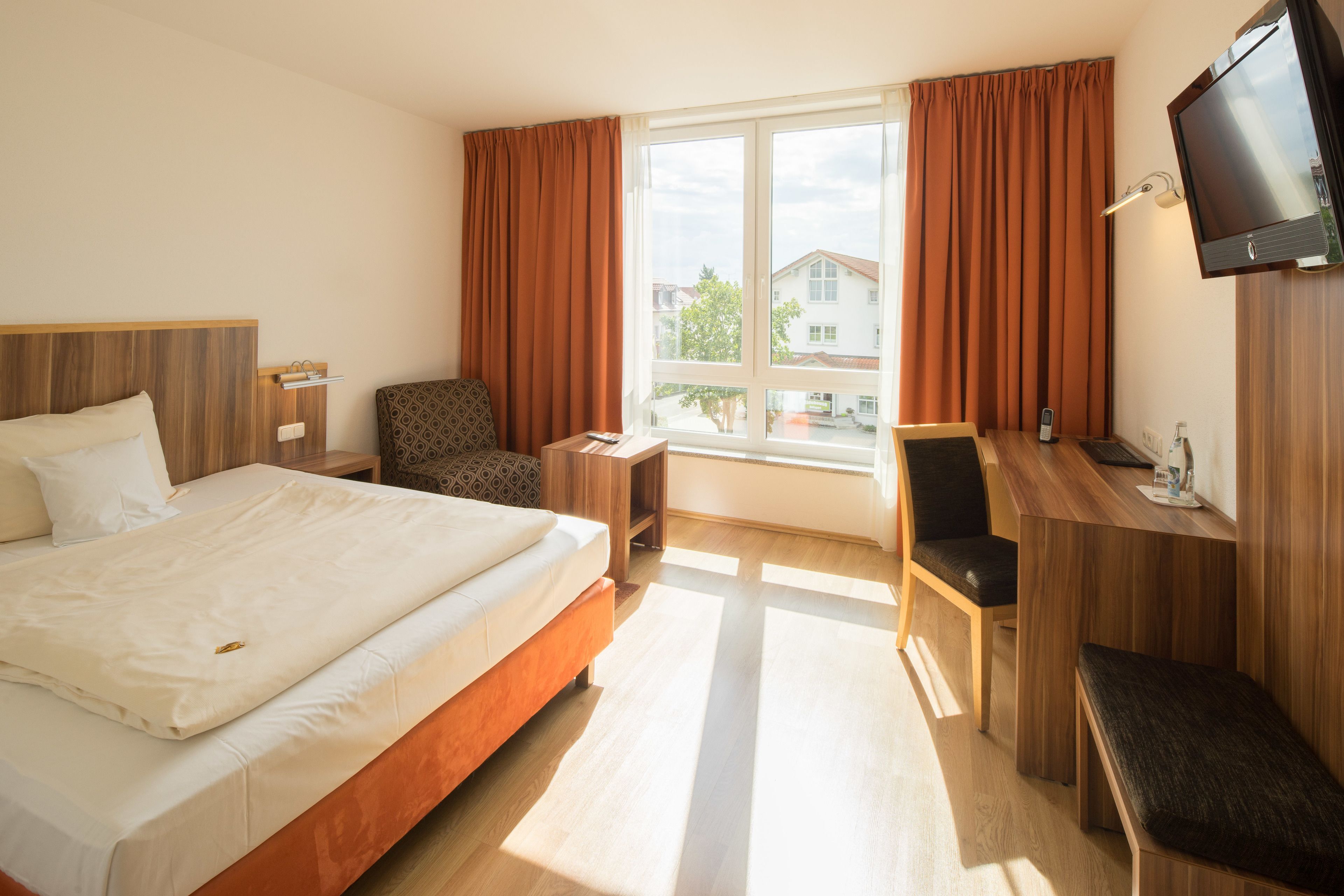 A hotel room with a bed, a desk, a chair, a TV, and a window with curtains.