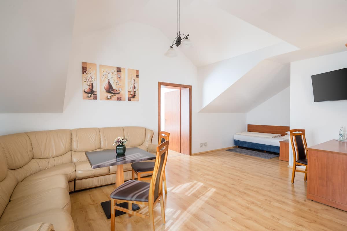 A modern loft apartment with a curved sofa, a dining table with chairs, a small bed, and a TV mounted on the wall.