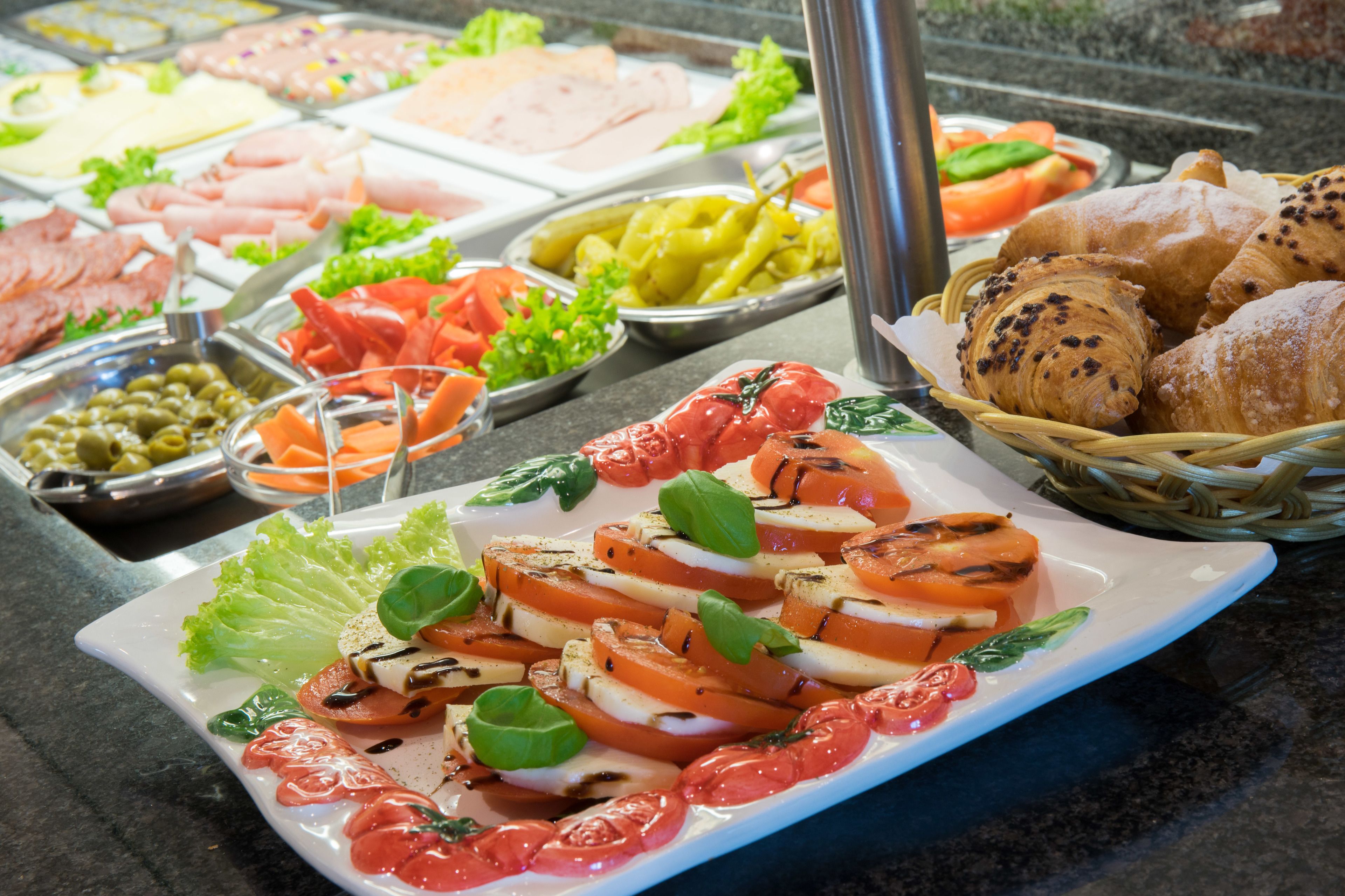 A buffet with various food options including sliced tomatoes, mozzarella, and a selection of meats.
