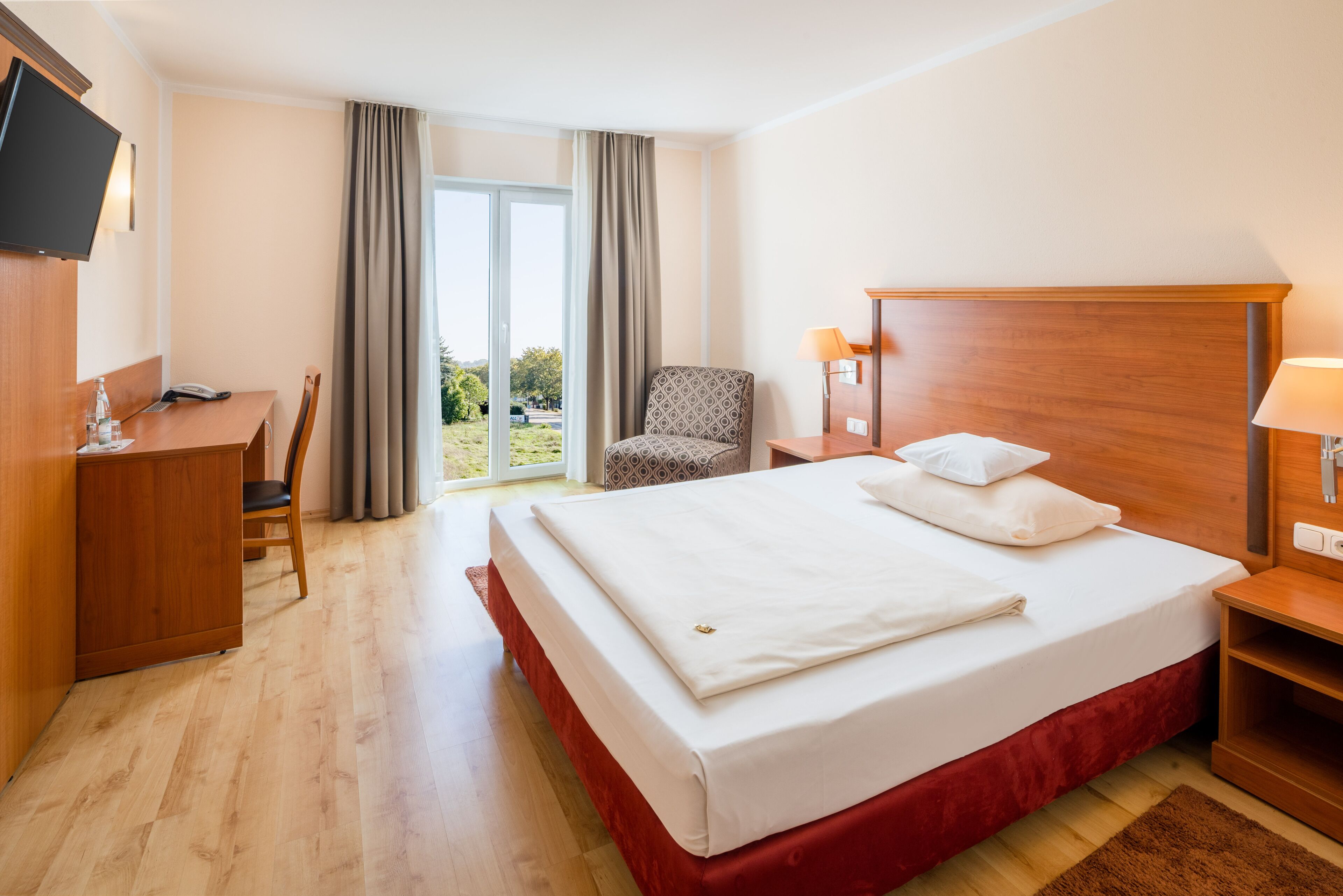 Una camera d'albergo con un letto grande, una scrivania, una sedia, una TV a parete e vista sull'esterno dalla finestra.