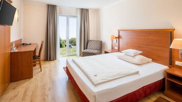Una camera d'albergo con un letto grande, una scrivania, una sedia, una TV a parete e vista sull'esterno dalla finestra.