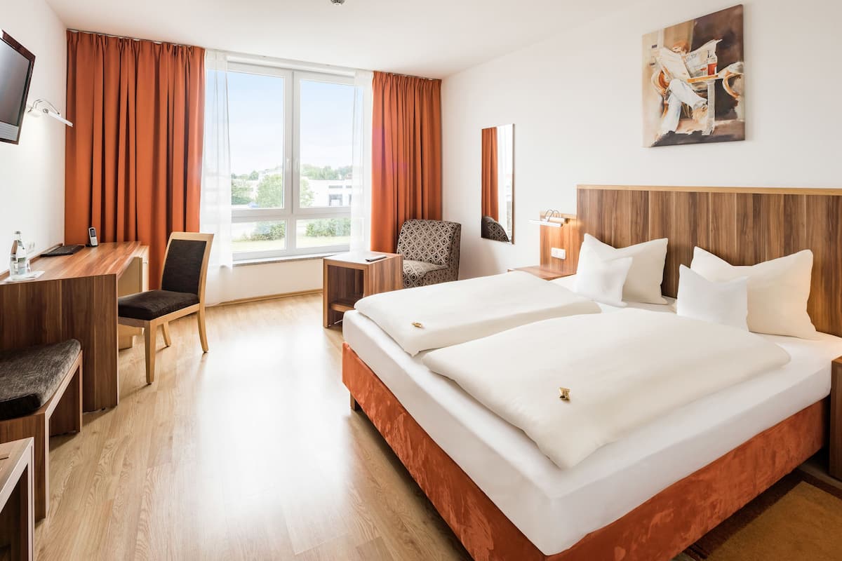 A hotel room with a large bed, a desk, a chair, and a TV.