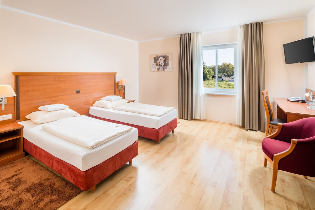 A hotel room with two beds, a desk, a chair, a TV, and a window with curtains.