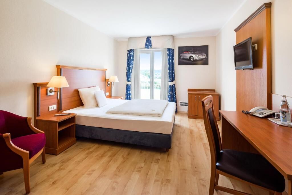 A hotel room with a bed, a desk, a chair, a TV, and a phone.