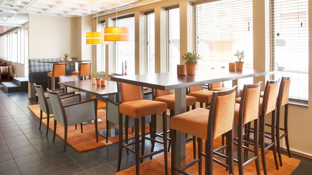 Un comedor moderno con una mesa larga, varios taburetes de bar y plantas en macetas.