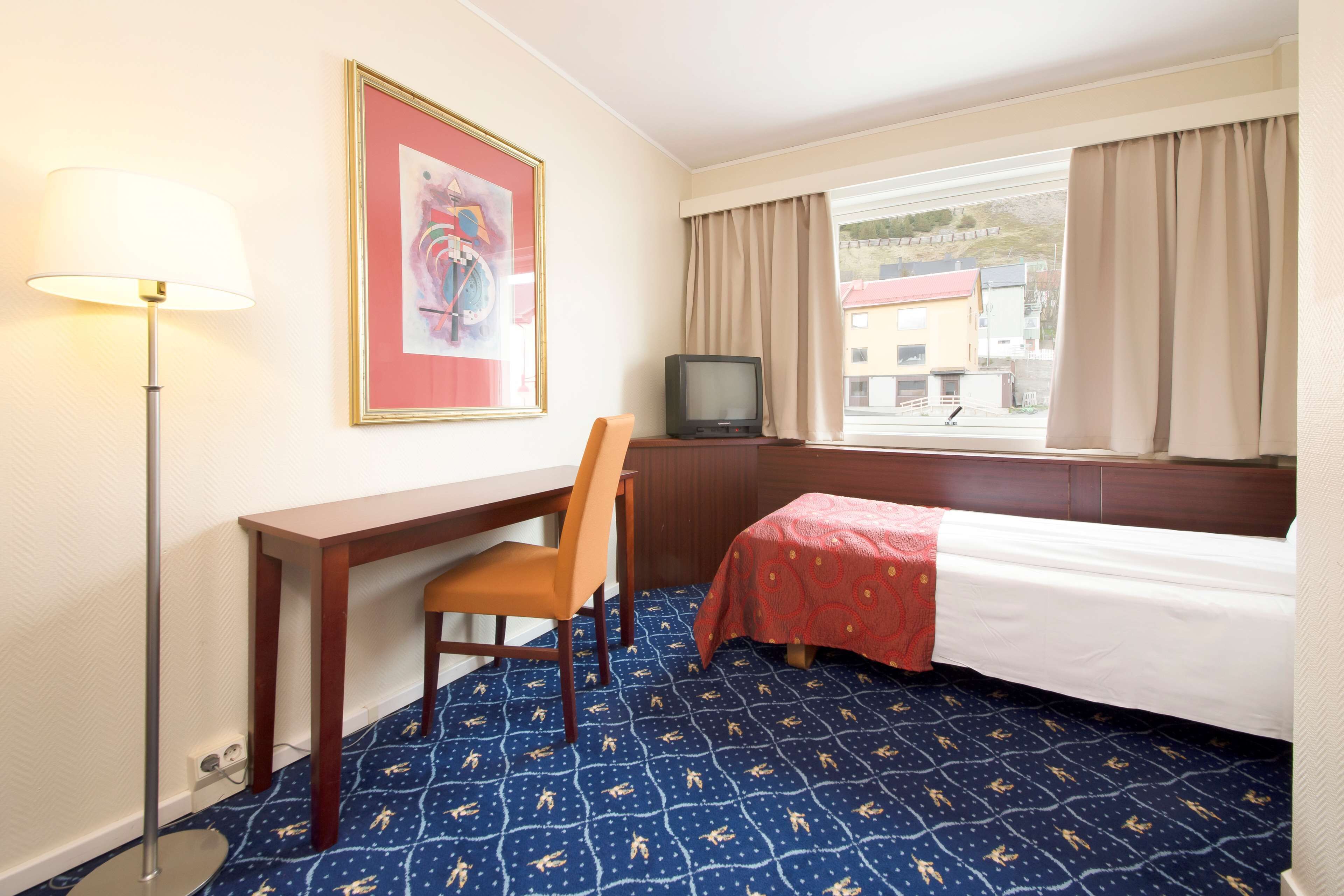 A hotel room with a bed, a desk, a chair, a television, and a window with curtains.