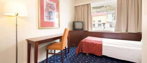 A hotel room with a bed, a desk, a chair, a television, and a window with curtains.