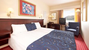 Una habitación de hotel con una cama grande, un escritorio con televisor y una silla.