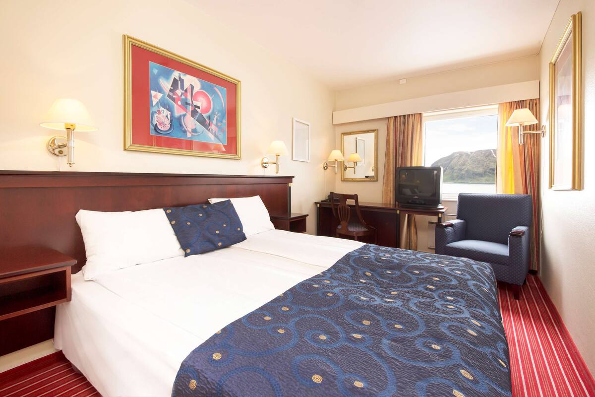 A hotel room with a large bed, a desk with a television, and a chair.