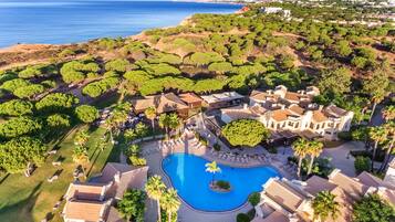 Vista aérea de un resort con una piscina central, rodeado de villas y exuberante vegetación.