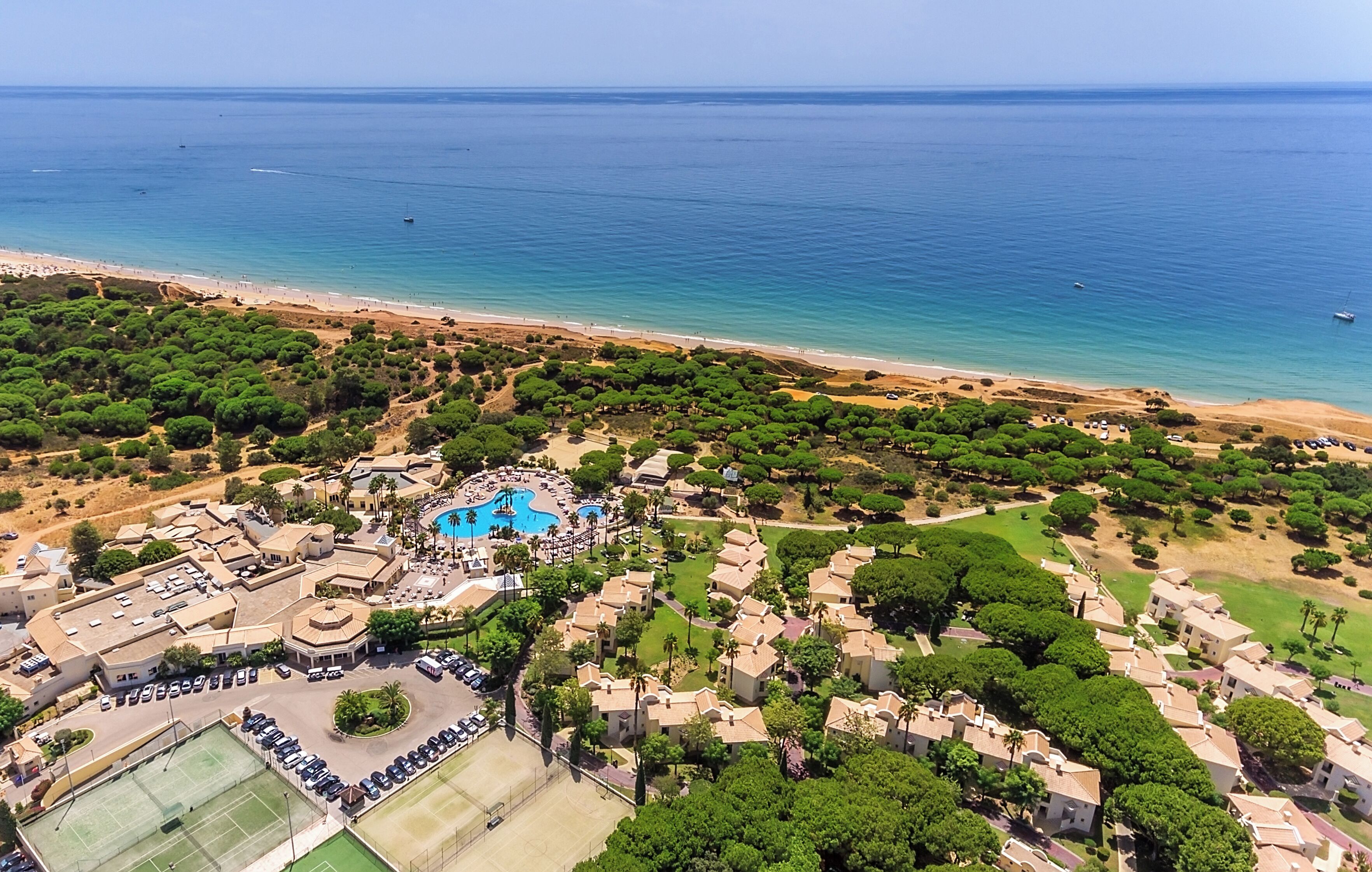 Oversigtsbillede af et resort med swimmingpool, strand og frodigt grønt område.
