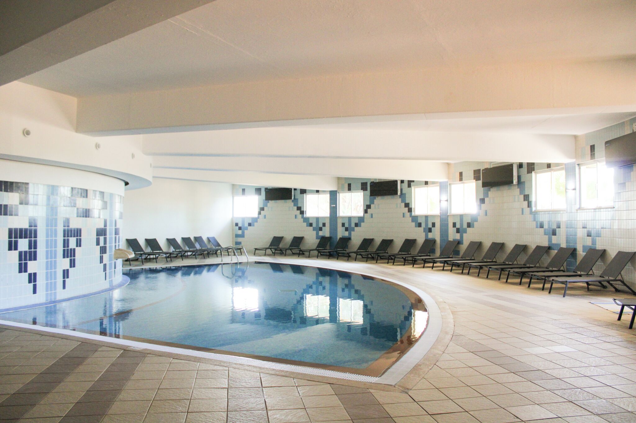 An indoor swimming pool with tiled walls and a tiled floor, surrounded by lounge chairs.
