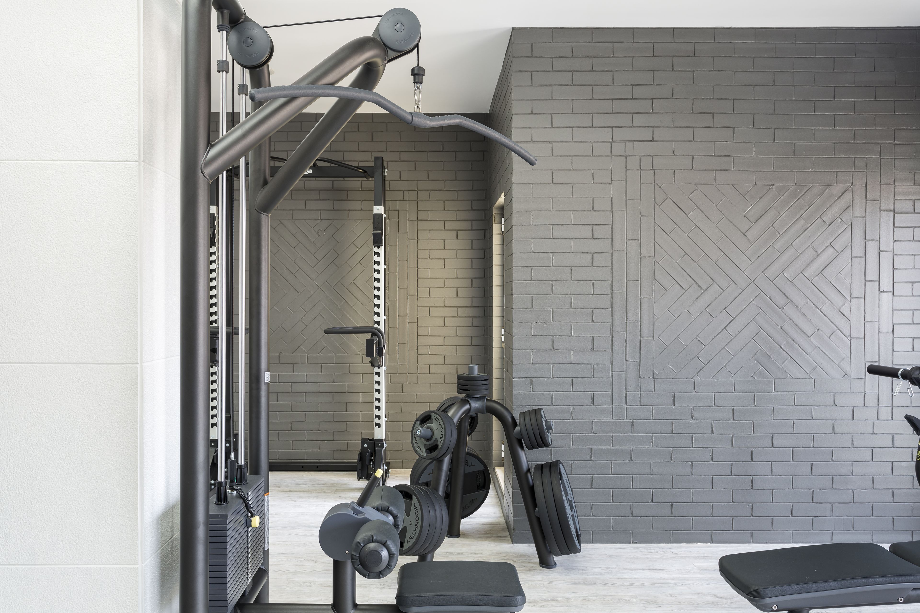 A gym with exercise equipment, a bench, and a brick-patterned wall.