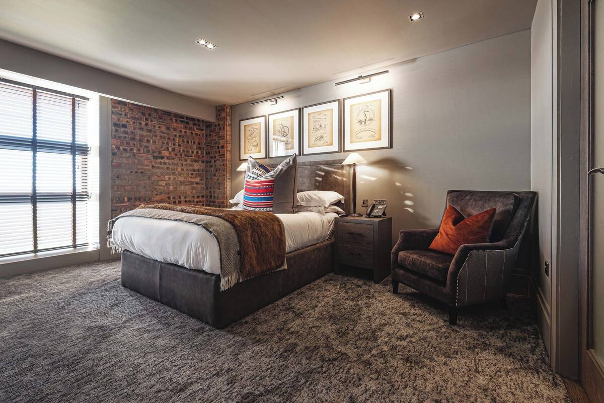 A bedroom with a large bed, a nightstand with a lamp, a chair, and framed pictures on the wall.