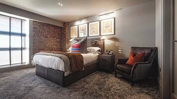 A bedroom with a large bed, a nightstand with a lamp, a chair, and framed pictures on the wall.