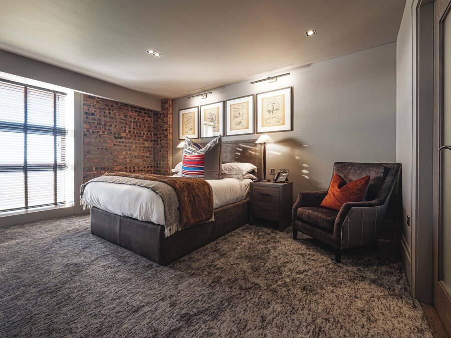 A bedroom with a large bed, a nightstand with a lamp, a chair, and framed pictures on the wall.