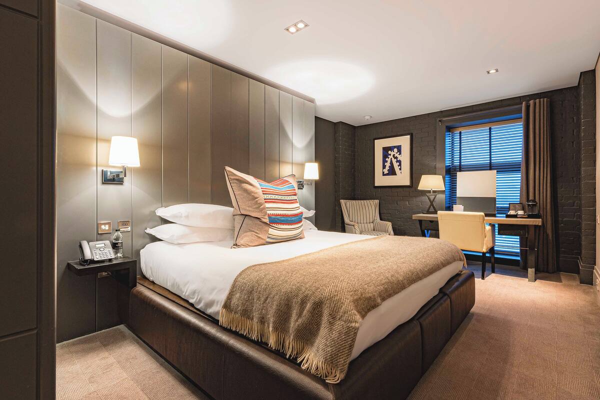 A modern hotel room with a large bed, bedside lamps, a desk, and a chair.