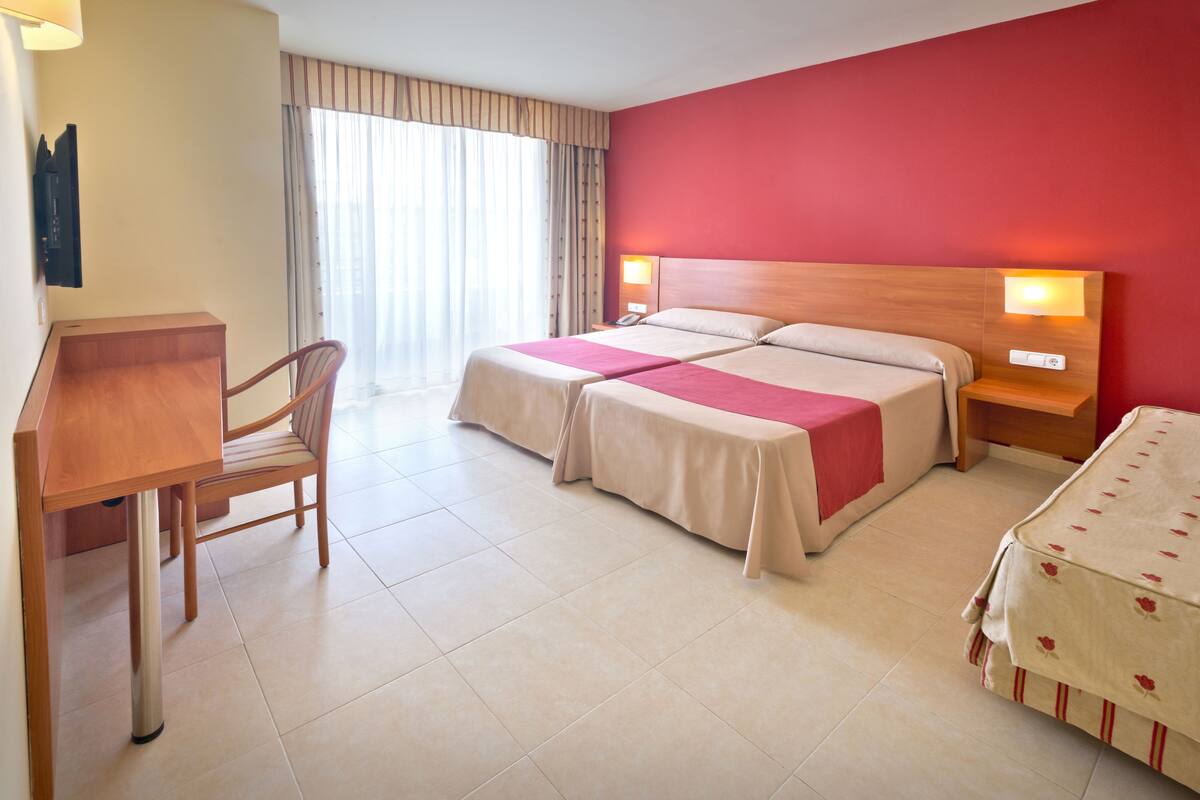 A hotel room with two beds, a desk, a chair, and a window with curtains.