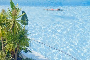 Una piscina cristalina con una persona nadando, rodeada de plantas tropicales.