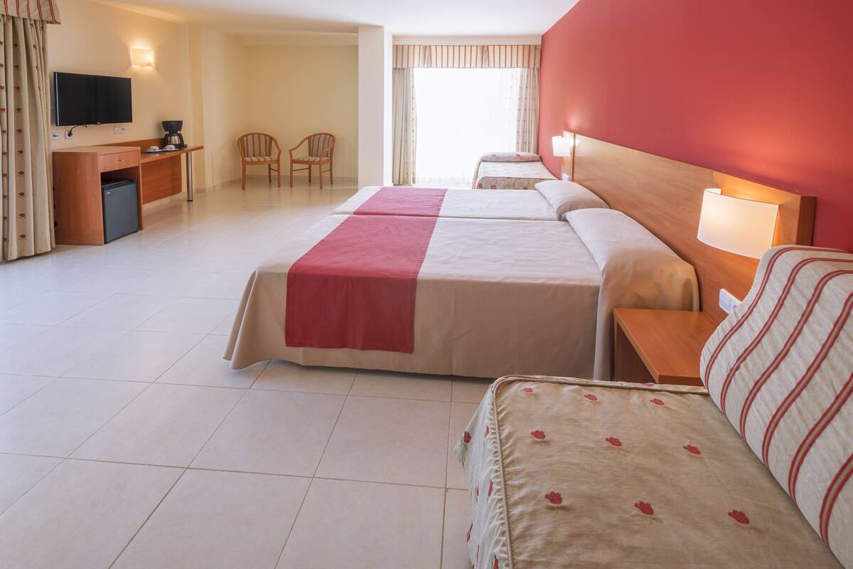 A hotel room with two beds, a desk with a television, a chair, and a small refrigerator.