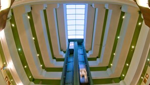 Une vue d’un atrium à plusieurs niveaux, avec un escalier mécanique central, des murs rayés de vert et de blanc, et une verrière au sommet.