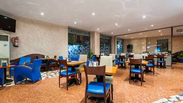 Un restaurante moderno con sillas y mesas en tonos azul y marrón, y un suelo con estampado.