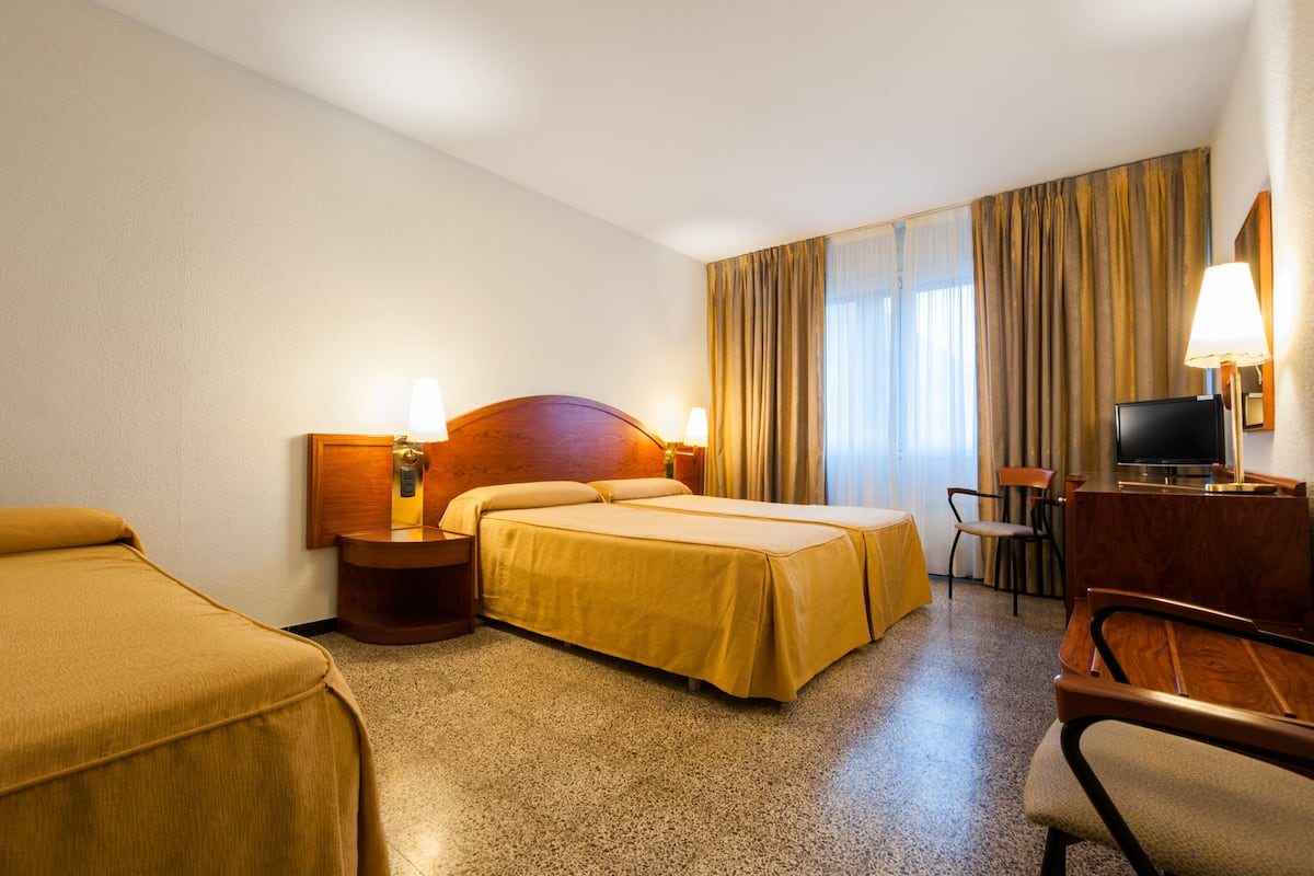 A hotel room with two beds, a desk, a chair, a television, and a window with curtains.