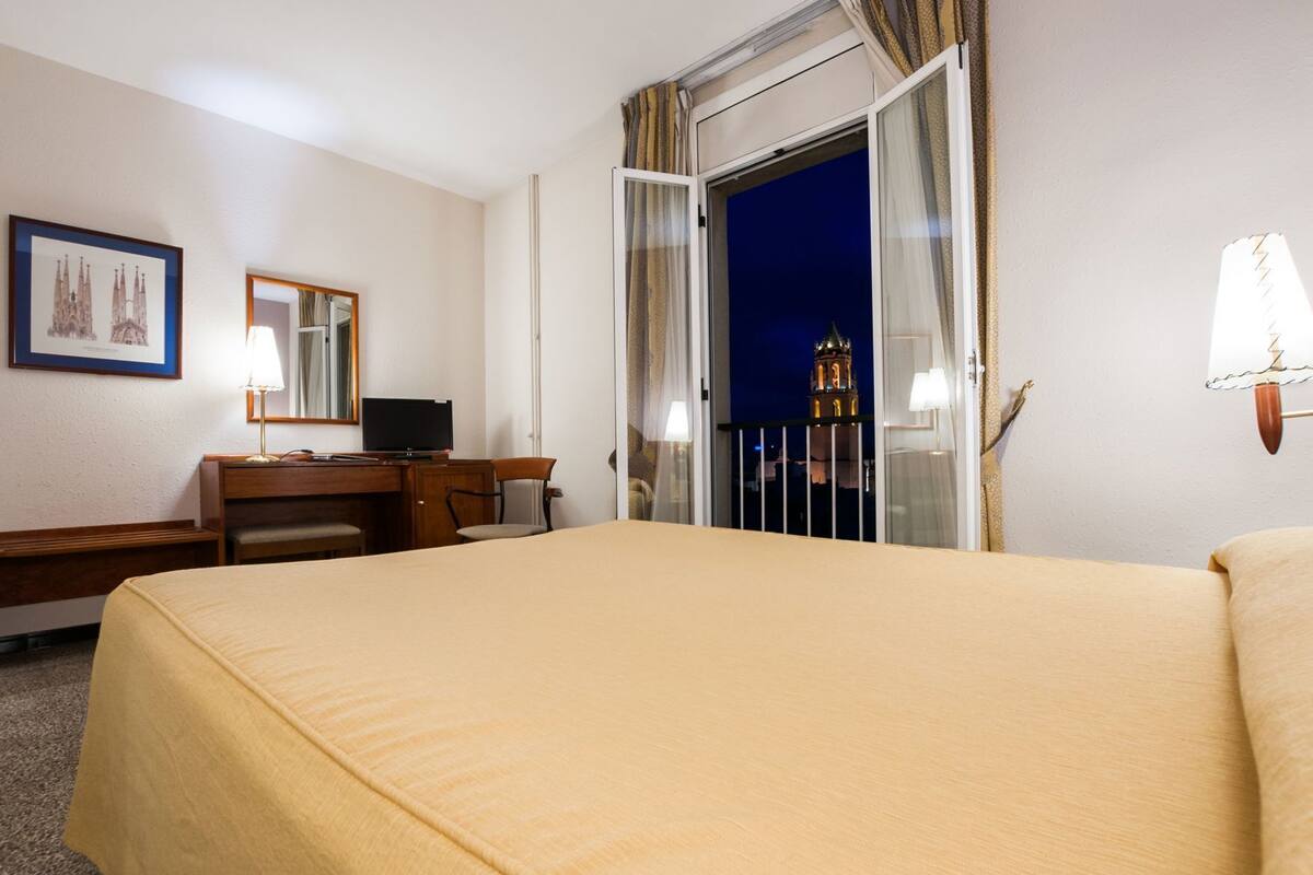 A hotel room with a bed, desk, chair, and a window with a view of a tower.