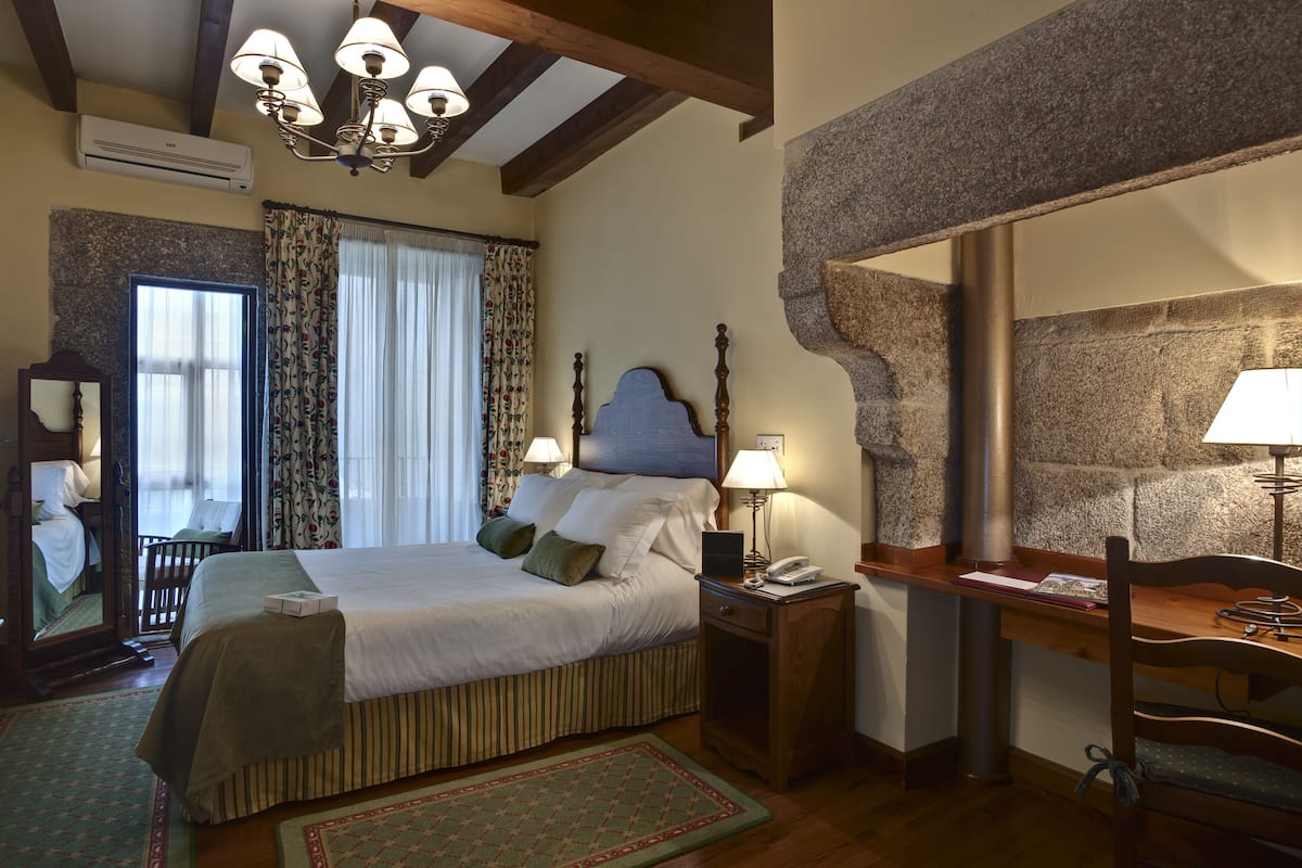 Une chambre d’hôtel avec un grand lit, un bureau avec une chaise, un miroir et un mur décoratif en pierre.