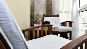 Una silla de madera con un cojín blanco, una mesita con un florero y una pared de piedra.