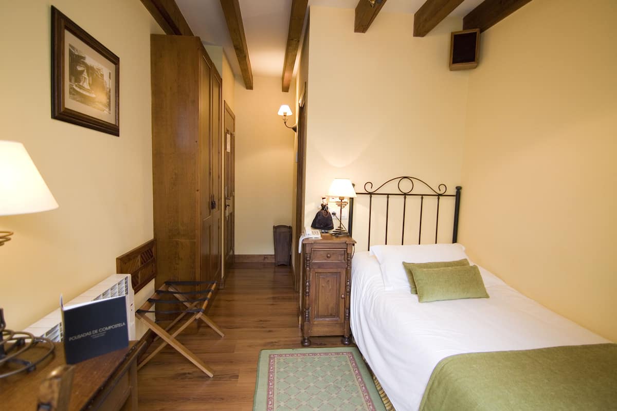 Une chambre à coucher avec un lit, une table de chevet, une lampe, une armoire en bois, un tableau encadré au mur et une petite table avec une boîte.