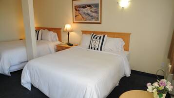 Quarto de hotel com duas camas, um quadro de uma paisagem costeira, abajur e um vaso com flores.