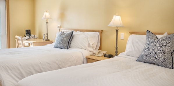 A hotel room with two beds, each with a white bedspread and patterned pillows. There are bedside tables with lamps and a small table with a coffee maker and a tray. - Smugglers Cove Inn (Lunenburg)