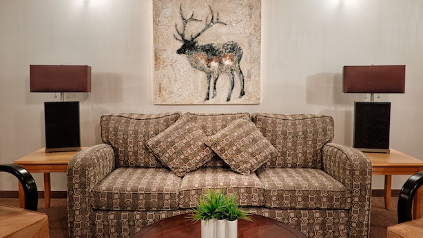 Een woonkamer met een gestreept bankje, twee bijzettafeltjes met lampen, en een schilderij van een hert aan de muur.