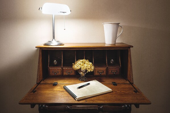 Un escritorio de madera con una lámpara, una taza, un florero con flores y una libreta.