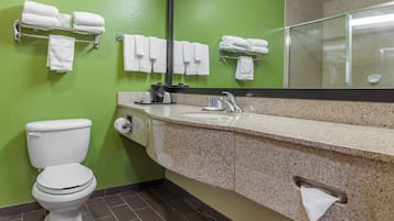 A bathroom with a green wall, a white toilet, a granite sink, and multiple towel racks.