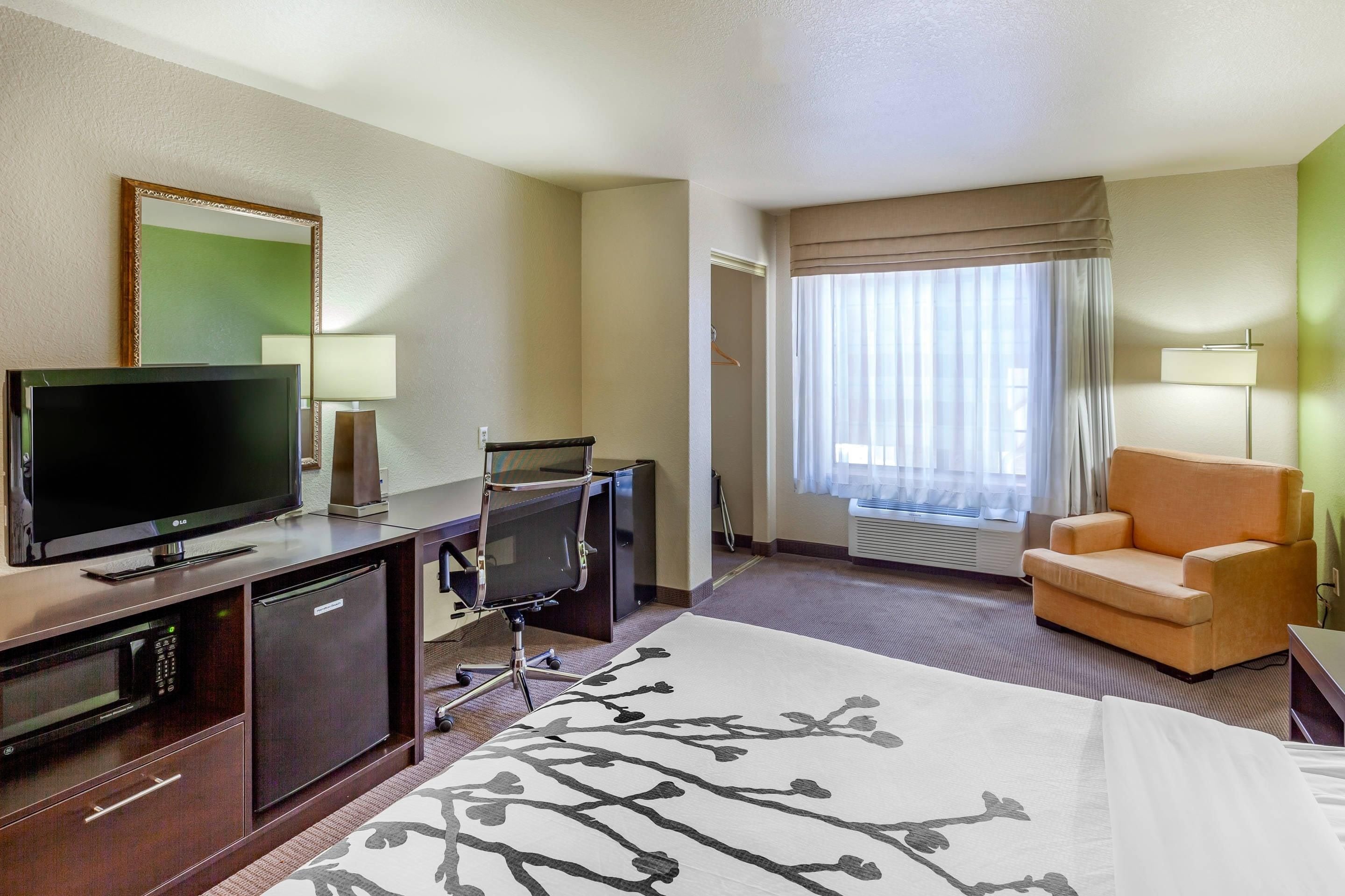 Une chambre d’hôtel comprenant un lit, une télévision, un bureau, une chaise, une fenêtre avec des rideaux et une lampe.