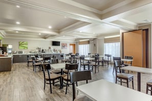 A spacious dining area with multiple tables and chairs, a kitchen area with modern appliances, and a large window providing natural light. - Sleep Inn & Suites Hewitt - South Waco (Hewitt)
