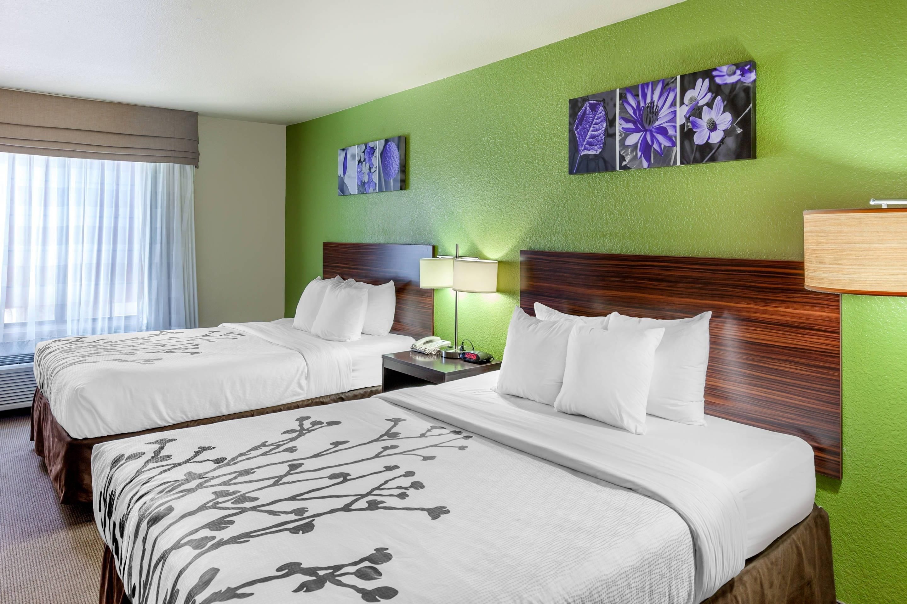 Een hotelkamer met twee bedden, een nachtkastje met een lamp, en een groene wand met bloemkunst.