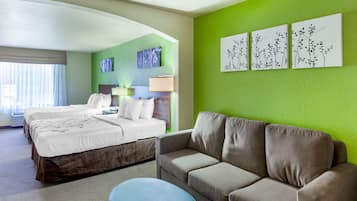 Quarto de hotel com cama, sofá, um banquinho azul e obras de arte nas paredes.